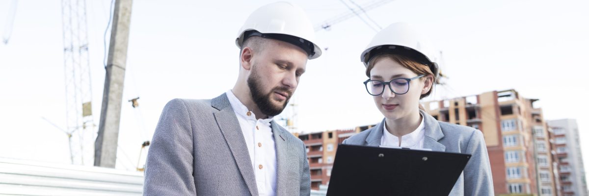 young-female-male-architect-wearing-hard-hat-looking-clipboard